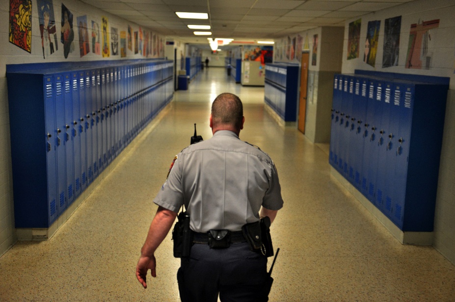 A security officer walking down a school hallway lined with lockers. 
