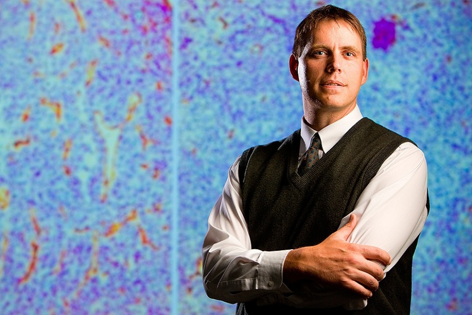 Joseph P. Balthasar posing in front of large image of a cell.