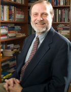 Lynn Kozlowski in a suit standing in front of a bookcase in his office. 