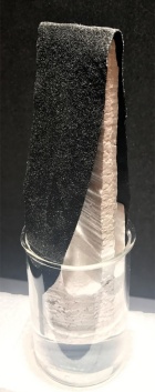 A piece of black paper draped in an upside-down "V", with edges hanging in a beaker holding water. 