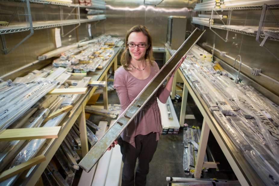 Elizabeth Thomas holds a long cylindrical sample of lakebed mud. The cylinder is sliced in half lengthwise to show the mud layers. 