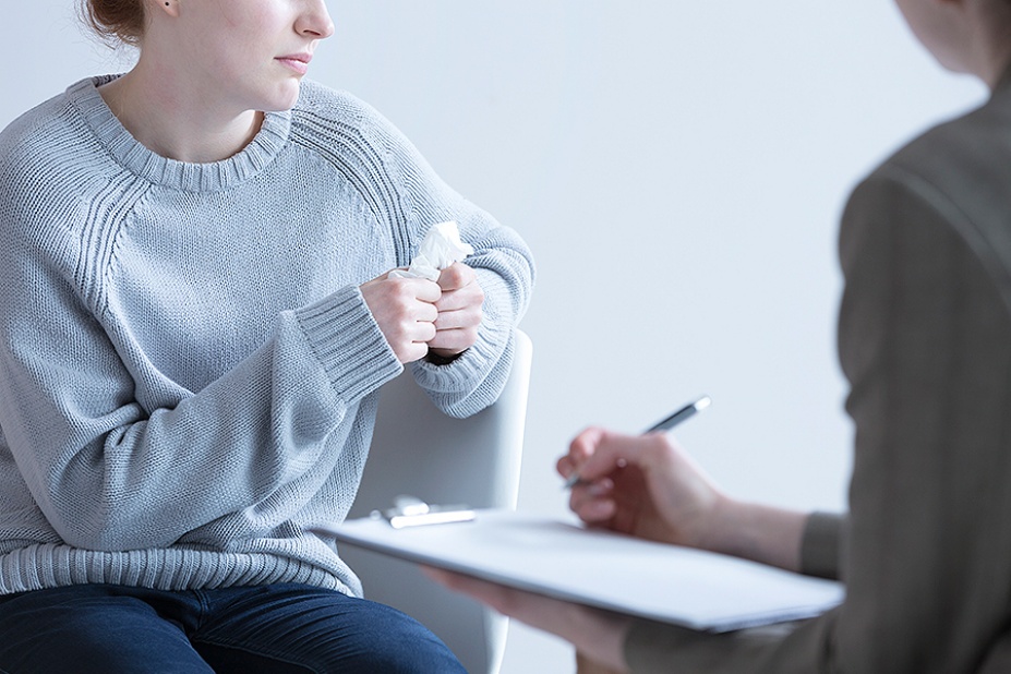 A woman with a clipboard and a pen talks with a woman holding a kleenex. 