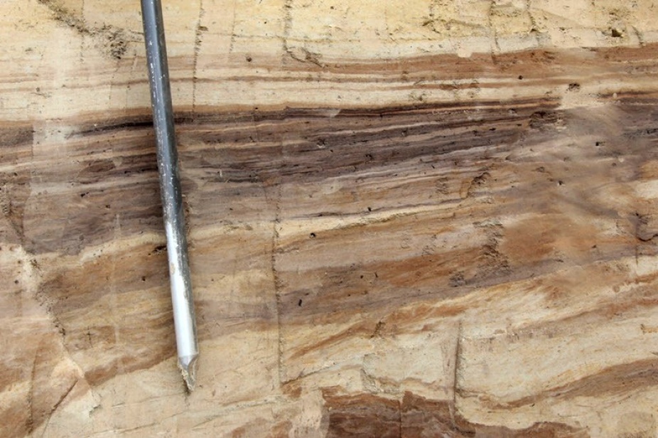 Zoom image: A close-up view of the sediment deposits reveals many layers of colorful material. The light-colored bands consist of windblown silt called loess, while the darker bands also hold ancient soil called paleosol. Credit: Elizabeth Thomas 