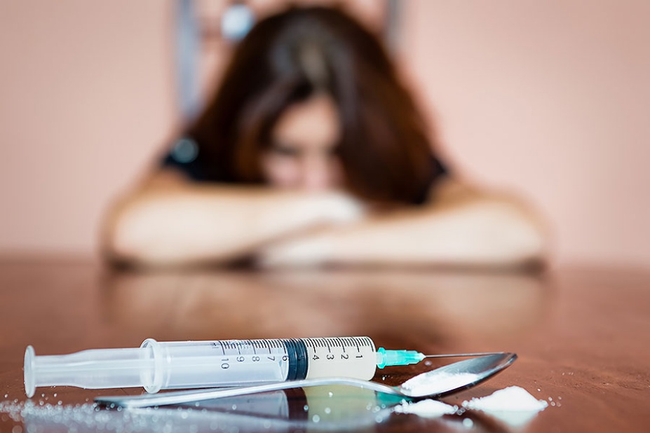 Syringe and drugs with in the foreground, female drug addict in the background.