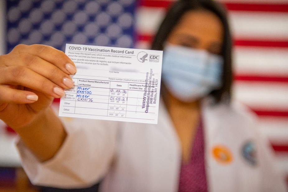 Person holding vaccination card in front of U.S. flag. 