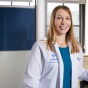 Jennifer Corliss, MD, standing, wearing white coat in front of window. 