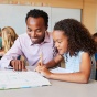 A Black teacher and student work together in a classroom. 