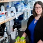 Chelsie Armbruster standing at the lab bench in front of shelf with many bottles. 