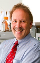 Portrait of a smiling man in a lab wearing a checked blue shirt and red tie. 
