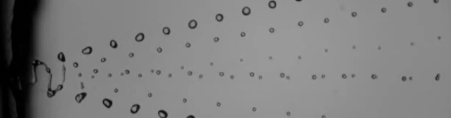 A black and white image showing aerosols fan out in unison from a source on the left. 