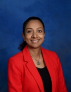Portrait of a woman wearing a black shirt and red blazer in front of a blue background. 