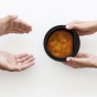 From above, one pair of hands gives another pair of hands a bowl of soup. 