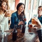 Two female friends together at a bar while speaking with men. 